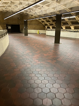 A picture of a metro station pathway. There are wayfinding structures slightly off center to the right and left, with the structure to the right being closer than the structure to the left. There are multiple half walls with railings on top of them in the image, with one to the left, one in the center of the background, and one to the right running from the background towards the foreground. A picture of a metro station pathway. There are wayfinding structures slightly off center to the right and left, with the structure to the right being closer than the structure to the left. There are multiple half walls with railings on top of them in the image, with one to the left, one in the center of the background, and one to the right running from the background towards the foreground.